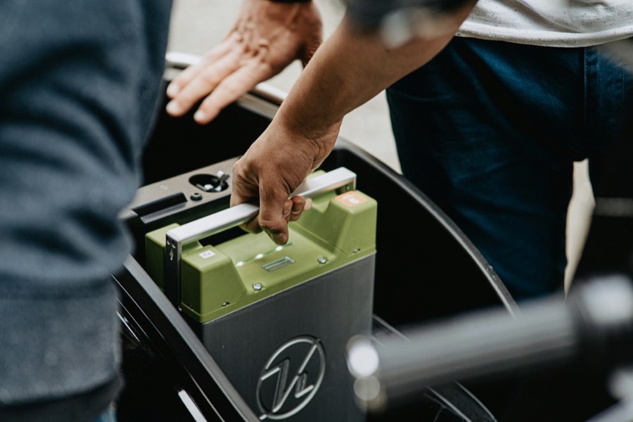 Hands swapping a green battery pack into an electric cargo bike