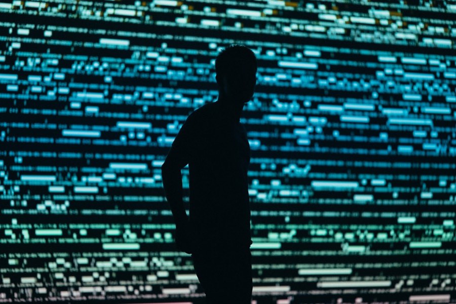 A person silhouetted against a large screen of dense scrolling data