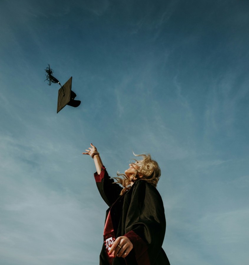 A graduate throwing a mortarboard into a bright open sky