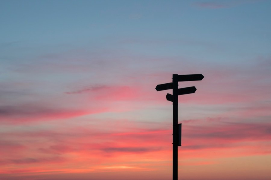 A signpost with three arms silhouetted against a red and blue sunset sky