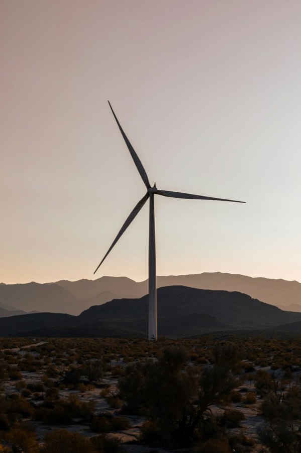 Wind turbine at dusk in front of desert mountains